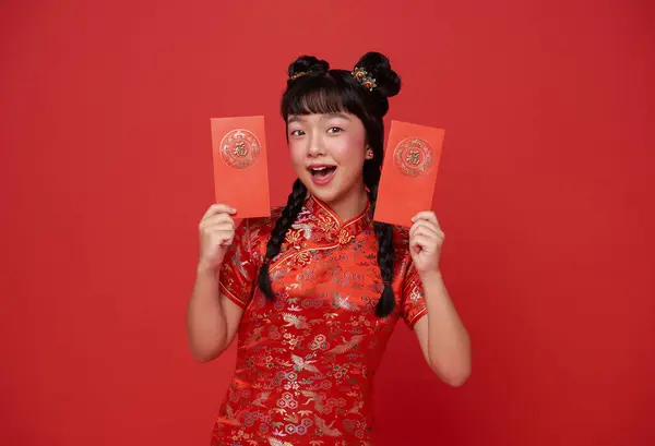 Happy Chinese new year. children asian girl wearing traditional qipao dress holding holding angpao or red packet monetary gift isolated on red background. Chinese text means great luck great happy.
