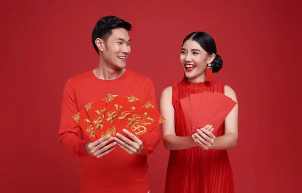 Happy Chinese new year. Asian couple wearing red clothing holding angpao or red packet monetary gift isolated on red background. Chinese text means great luck great happy.