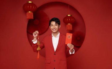 Yeni Çin yılın kutlu olsun. Elinde angpao ya da kırmızı para paketi olan Asyalı bir adam kırmızı dekorasyon arka planında izole edilmiş. Çince yazılar büyük şans demektir..