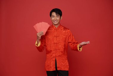 Mutlu Çin Yeni Yılı 2024. Kırmızı geleneksel kıyafetler giyen Asyalı bir adam angpao ya da kırmızı arka planda izole edilmiş para paketi taşıyor.. 