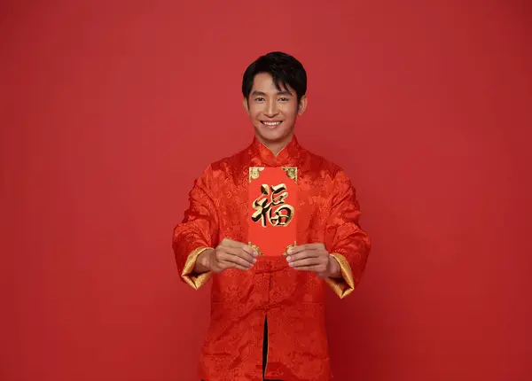 Happy Chinese new year 2024. Asian man holding angpao or red packet monetary gift isolated on red background. Chinese text means great luck great happy.