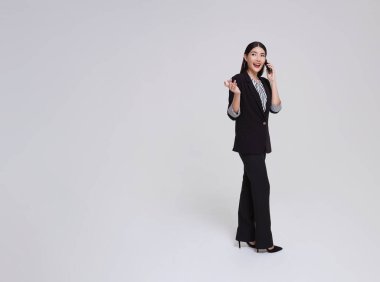 Takım elbiseli mutlu Asyalı iş kadınının tam boy portresi gri arka planda izole edilmiş ürün için fotokopi alanıyla iletişim kuruyor..