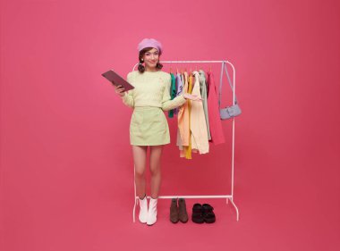 Perakende mağaza kıyafetleri içinde kontrol listesi olan Asyalı moda yöneticisi ya da pembe arka planda izole edilmiş kıyafet denetimi. Girişimci, alışveriş ve hisse senedi yazan küçük işletme sahibi 