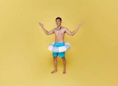Tam vücut genç turist Asyalı adam şişme yüzük tutuyor. Sarı arka planda izole edilmiş mutlu yaz tatili..