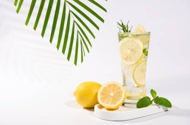 Beyaz masa arkasında taze yapılmış limonata, buz küpleri ve limon meyveleri..