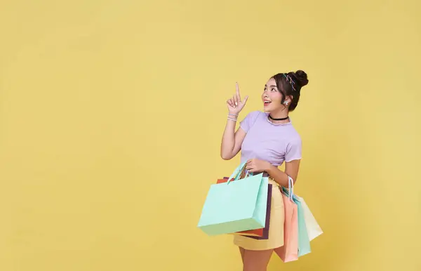 Glückliche Hübsche Asiatische Frau Trägt Bunte Einkaufstüten Und Zeigt Mit lizenzfreie Stockfotos