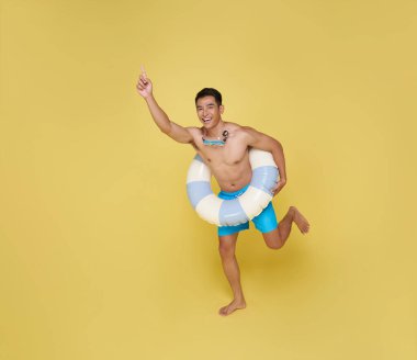 Tam vücut genç turist elinde şişme yüzük, atlayan mutlu yaz tatili plaj partisi sarı arka planda izole edilmiş..