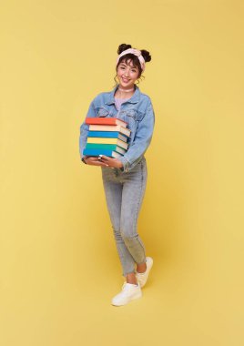 Mutlu gülümseyen Asyalı üniversite öğrencisinin portresi okula hazır sarı arka planda izole edilmiş kitapları tutuyor..