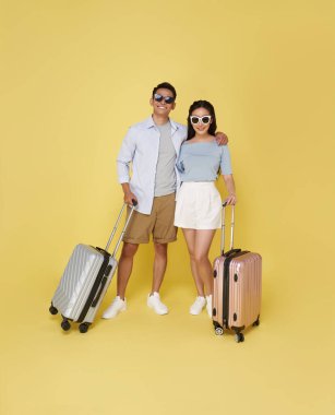 Mutlu Asyalı çift seyahat için bavullarıyla seyahat ederken sarı stüdyo arka planında izole edilmiş..