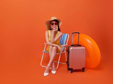Yaz tatili zamanı. Genç bir kadın, turuncu arka planda, yaz tatilinde güverte koltuğunda rahat ve mutlu bir şekilde oturuyor. Seyahat ve yaşam tarzı kavramı
