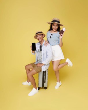 Mutlu Asyalı çift seyahate çıkıyor. Sarı arka planda izole edilmiş seyahat için pasaportlu telefonları var..