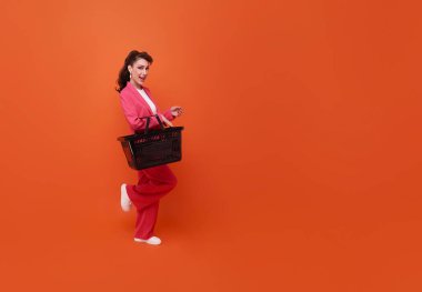 Gülümseyen ve elinde alışveriş sepeti tutan güzel bir kadın fotokopi alanı turuncu arka planında izole edilmiş, tam uzunlukta insan kompozisyonu