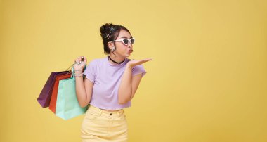 Sarı stüdyo arka planında izole edilmiş renkli alışveriş çantaları taşıyan mutlu Asyalı kadın..