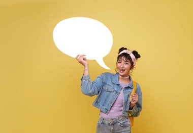 Neşeli genç Asyalı kadın ayakta duruyor ve elinde beyaz boş afiş panosu, sarı arka planda reklam panosu taşıyor..