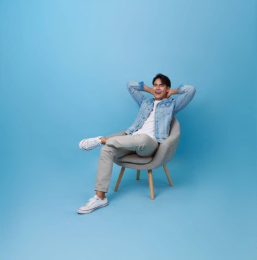 Asyalı yakışıklı adam mavi arka planda izole bir şekilde kanepede rahatlıyor..