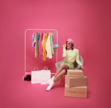 Pembe arka planda izole edilmiş moda mağazası alışveriş merkezinde mutlu Asyalı genç kadın kıyafetleri..