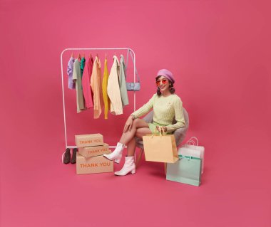 Pembe arka planda izole edilmiş moda mağazası alışveriş merkezinde mutlu Asyalı genç kadın kıyafetleri..