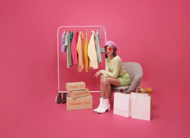 Pembe arka planda izole edilmiş moda mağazası alışveriş merkezinde mutlu Asyalı genç kadın kıyafetleri..