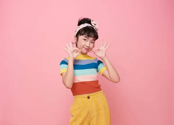 stock image happy Asian cute girl showing OK gesture smiling isolated on pink background.