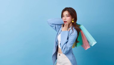 Mutlu, güzel Asyalı kadın mavi fotokopi arkaplanda izole edilmiş renkli alışveriş çantaları taşıyor..