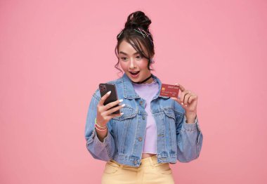 Mutlu Asyalı genç alışveriş yapan kadınlar pembe arka planda izole akıllı telefonlarıyla online alışveriş için kredi kartı ödemeleri yapıyorlar..