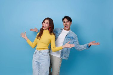 Şaşırmış Asyalı çift gülümsüyor ve mavi stüdyo arka planında el ele tutuşuyor..