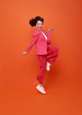 Mutlu, güzel bir kadın gülümseyip zıplarken başarıyı kutluyor turuncu arka planda..