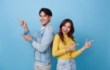 Mutlu Asyalı çift, mavi stüdyo fotokopi arkaplanında izole edilmiş ürünler için el işareti yapıyor ya da yapıyor..