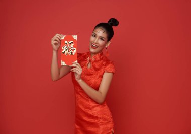 Yeni Çin yılın kutlu olsun. Geleneksel Cheongsam Qipao elbisesi giyen Asyalı bir kadın angpao ya da kırmızı paketli bir hediye taşıyorsa büyük şans ve kırmızı arkaplanda büyük kâr demektir..