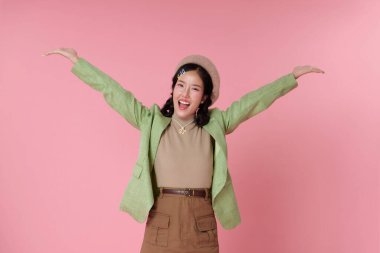 Mutlu Asyalı kadın kollarını açmış gülümsüyor, pembe arka planda izole edilmiş neşe ve açıklığı ifade ediyor..