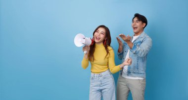 Genç, sevimli Asyalı bir çift ellerinde megafonla bağırarak mavi fotokopi arkaplanında izole edilmiş bir duyuru yapıyor. reklam ve duyuru konsepti.