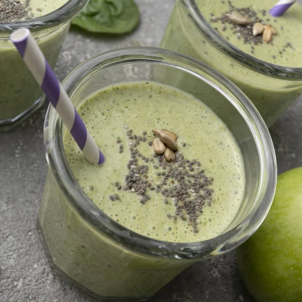 Healthy green spinach smoothie in glass jars and other ingredients on a gray concrete background. Superfoods, detox, diet, healthy food. Celery, apple, spinach, spinach, and banana.