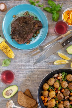 Ev yapımı yemekler, sebzeler, otlar, tavada kızarmış biftek ve yeni patateslerle dolu bir yemek masası.