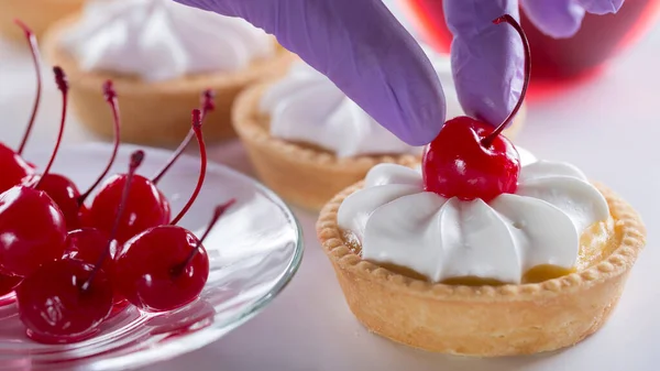 A woman pastry chef decorates a cake with a cocktail cherry. Production of pastries and cakes.