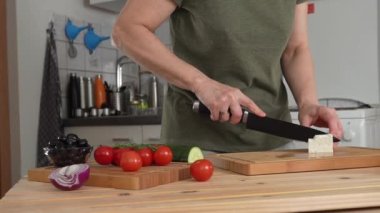 Ev mutfağında Yunan salatası için peynir kesen kadın.