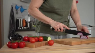 Ev mutfağında Yunan salatası için kırmızı soğan kesen kadın.