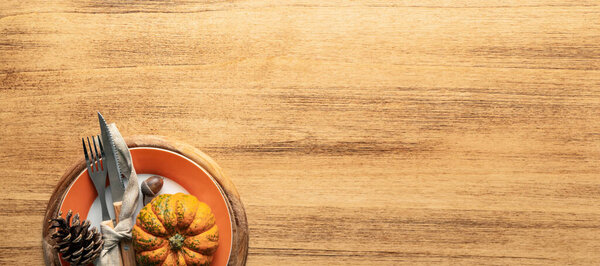 A plate with cutlery is decorated for Thanksgiving with pumpkins and autumn products on a wooden table, top view