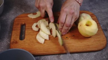 Woman hands slicing apples on a wooden cutting board close-up on a kitchen table