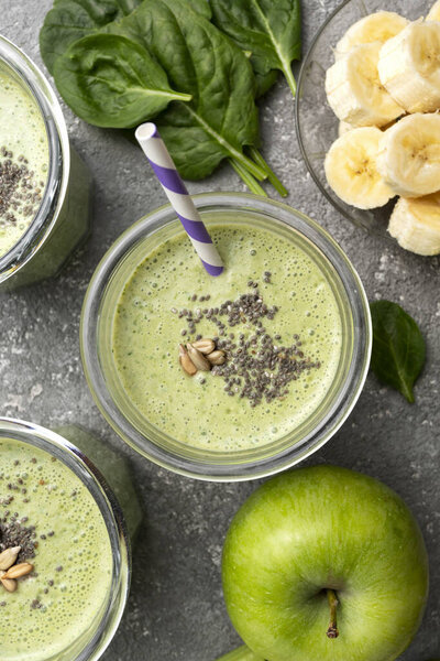 Детоксикационный шпинат напиток с зеленым яблоком и бананом, на сером бетонном фоне в очках, вид сверху