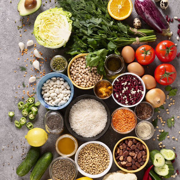 Large set of balanced nutrition products on gray concrete background, top view. Vegetables, fruits, nuts, grains, olive oil, green herbs.