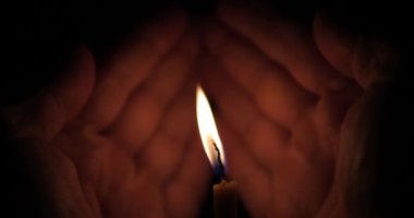 Avuçlarda bir anıt mum. Mum alevi ellerle rüzgardan korunur. Karanlıkta bir mum.