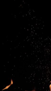 Siyah arka planda alevler ve kıvılcımlar. Büyük bir şenlik ateşi. Ateş ve tehlike. Şöminede odun yakmak. Romantik yangın. Geceleri yangın. Dikey video. doku.