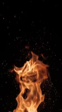 Siyah arka planda alevler ve kıvılcımlar. Büyük bir şenlik ateşi. Ateş ve tehlike. Şöminede odun yakmak. Romantik yangın. Geceleri yangın. Dikey video. doku.