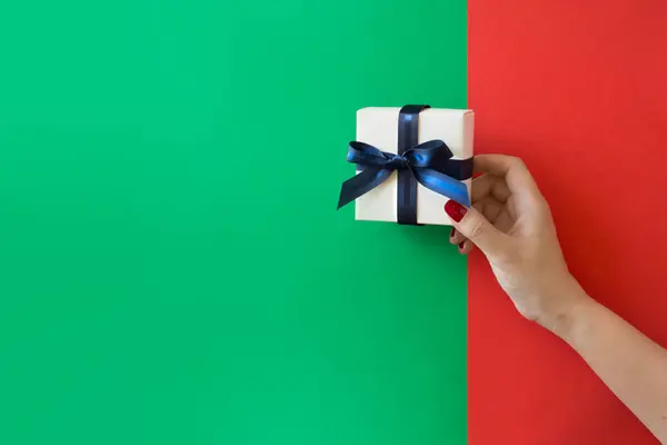 Hand Hält Eine Geschenkbox Auf Rotem Und Grünem Hintergrund lizenzfreie Stockfotos