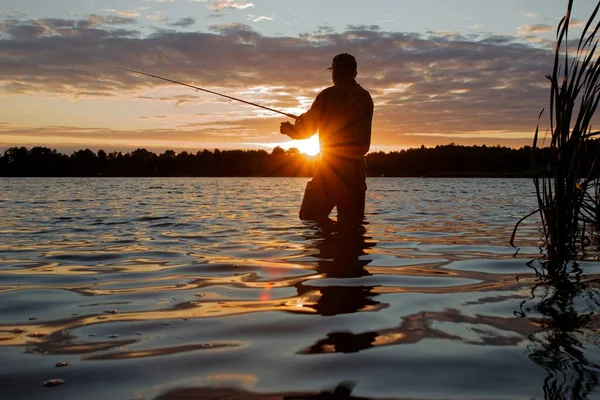 日落时带着镜头照明弹缺陷站在湖中钓鱼的渔民 — 图库照片