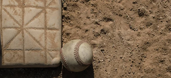 Baseball ball by base on dirt sports field close up, copy space on banner background