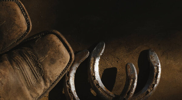 Western lifestyle with cowboy boots and horseshoes on old wood retro rustic background.