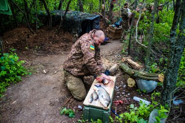 28. Topçu Taburu 'ndan Ukraynalı asker cephe hattının yakınındaki bir gölette yakalanan balıkları pişiriyor. Askerler, savaşın olduğu yerdeki taze ürünleri depolamak için bir dakikalık dinlenme fırsatından yararlanıyorlar.