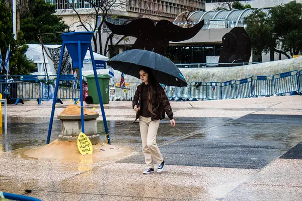 Tel Aviv, İsrail, 18 Şubat 2024 İsrail 'in sembolik ve simgesel şehri Tel Aviv sokaklarında şemsiyeyle yürüyen insanlar