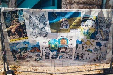 Kharkiv, Ukrayna, 27 Ağustos 2025. Savaş felaketlerini resmeden çocukların çizimleri, Rus füze saldırısının ardından hasar gören bir binanın çalışmalarını gizleyen brandalara basılmıştır..